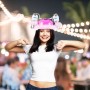 Lachende Frau mit pinkem Bierhelm, 2 Dosenhaltern und rosa Federboa auf einer Party. Ideal für Festivals.