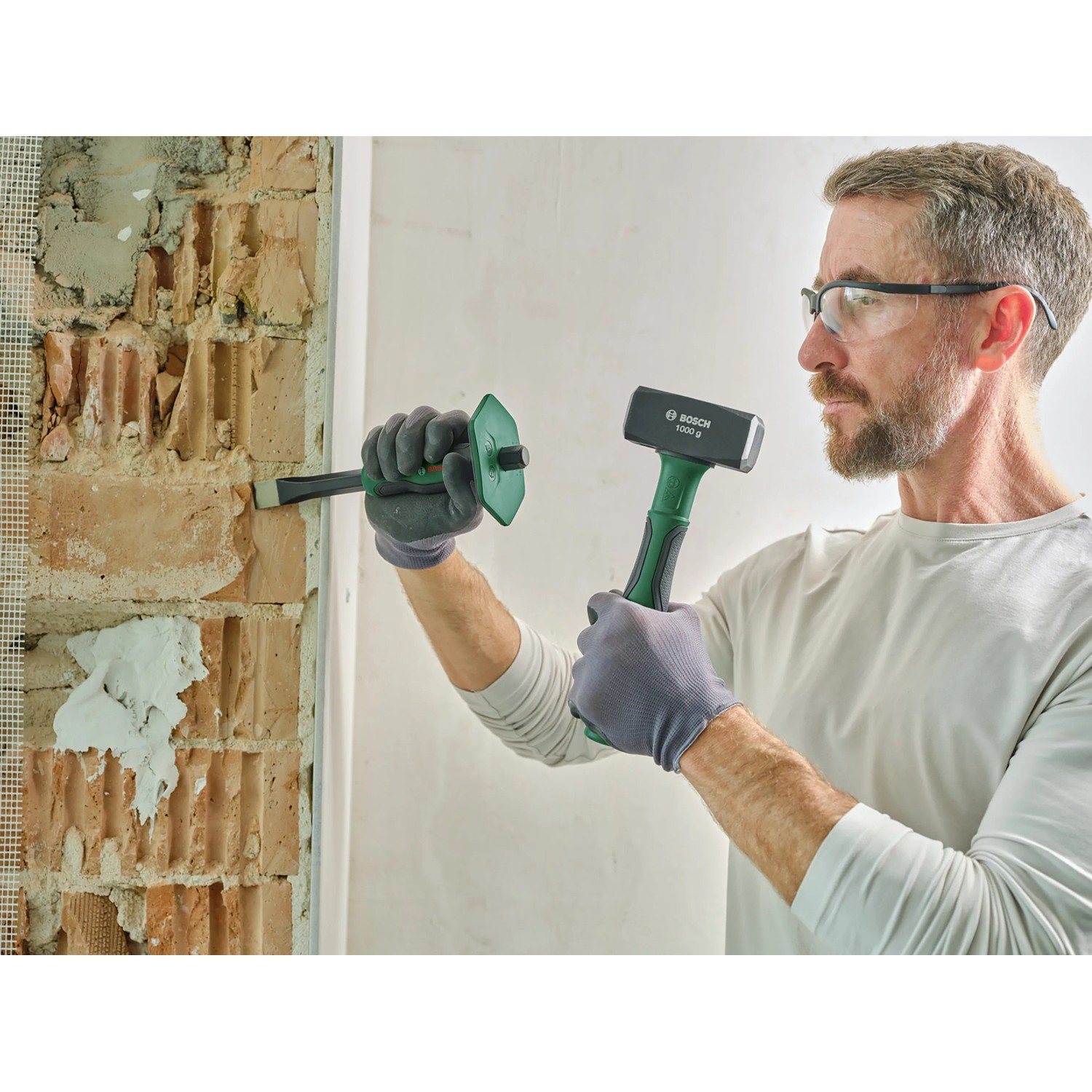 Mann beim Stemmen einer Wand mit Bosch Fäustel (1 kg) und Meißel. Hammer der Kategorie Hämmer.