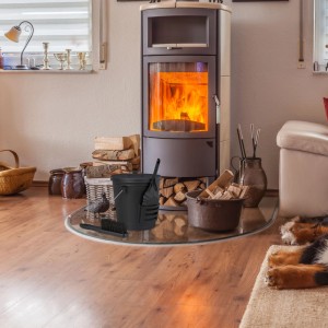 Schwarzer Relaxdays Ascheeimer aus Stahl mit Deckel, Schaufel und Besen vor Kamin.