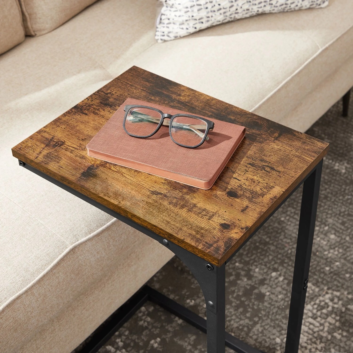 Vasagle Beistelltisch in C-Form, braun-schwarz, mit Buch und Brille auf der Tischplatte.