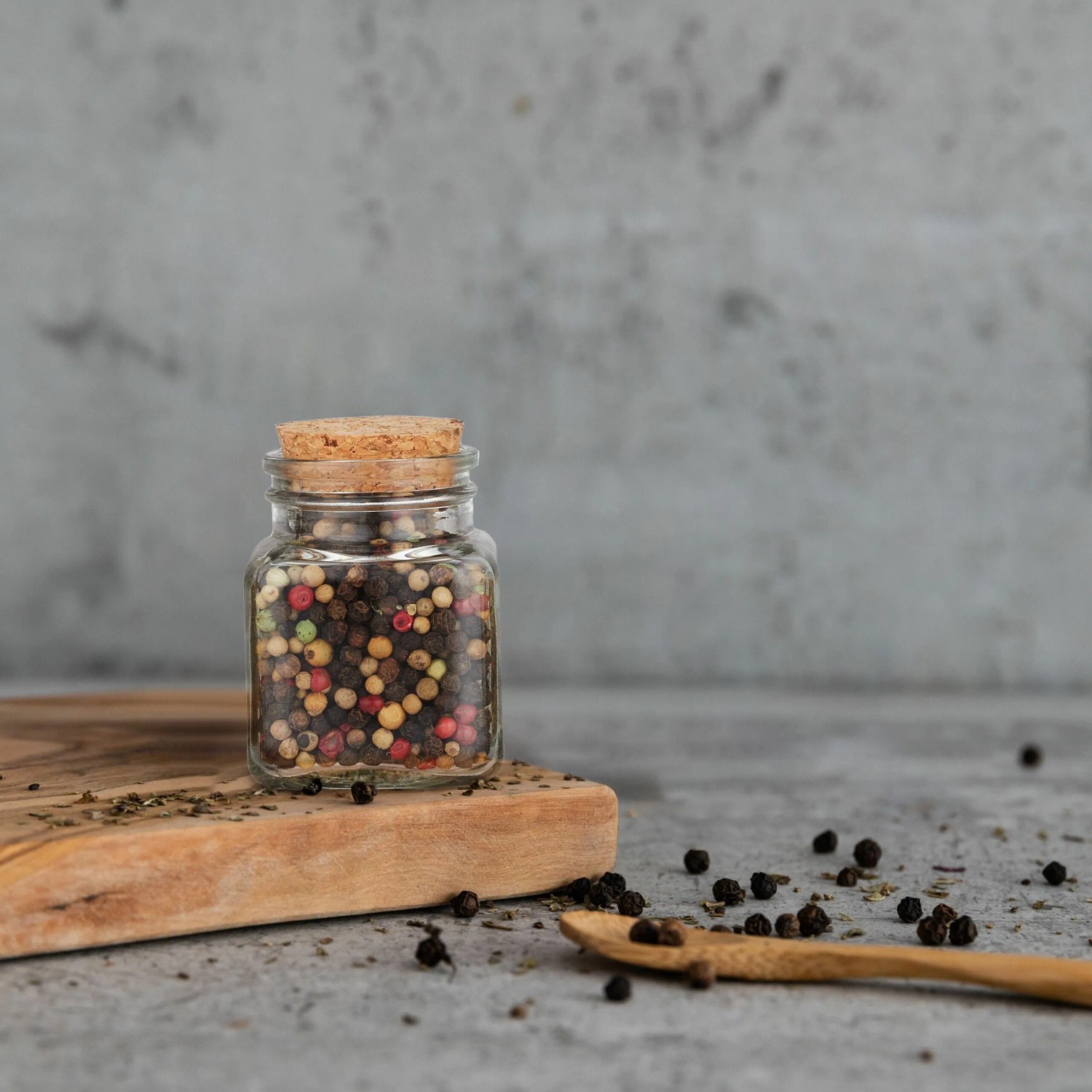 Transparentes Gewürzglas mit Korkdeckel, gefüllt mit Pfeffer, auf Holzbrett. Teil des 20er Sets für Küchenorganisation.