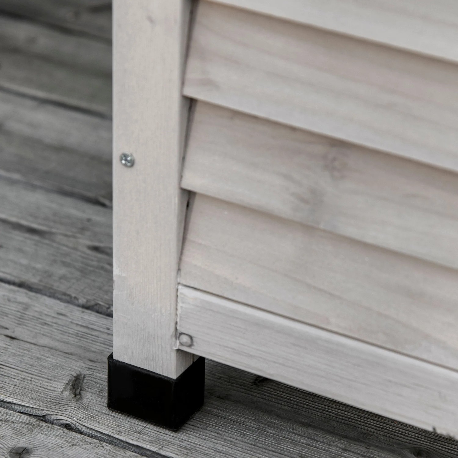 Detailansicht der grauen Holz Gartenbox: Lamellenwand und schwarzer Fuß auf Holzterrasse. Stabile, wetterbeständige Aufbewahrung.