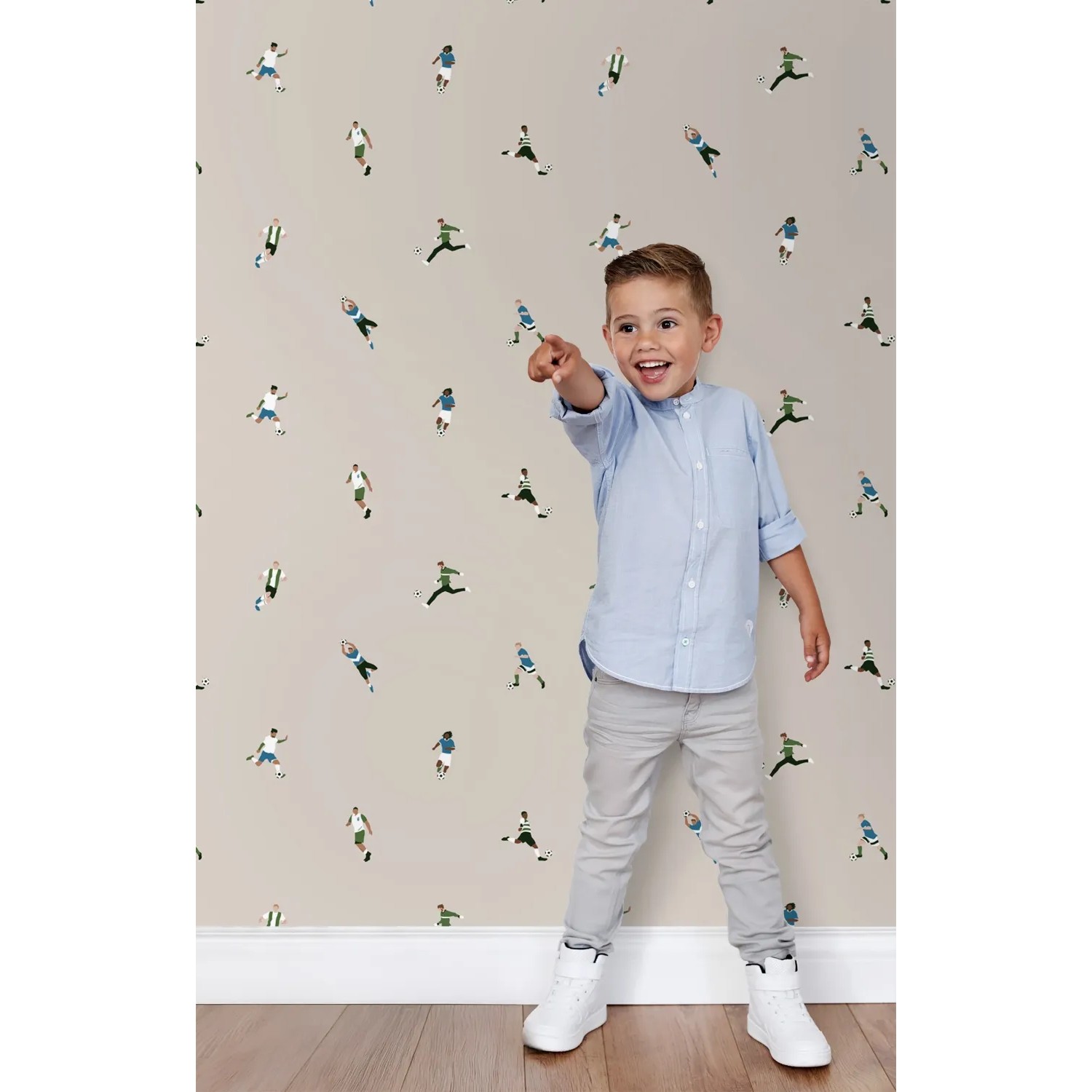 ESTAhome Vliestapete mit beigen Fußballspielern. Ein Kind zeigt auf das fröhliche Muster an der Wand im Kinderzimmer.