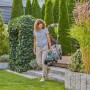 Frau trägt Gardena Akku-Rasenmäher PowerMax 32/18V im Garten. Kompakter Rasenmäher mit Akku.