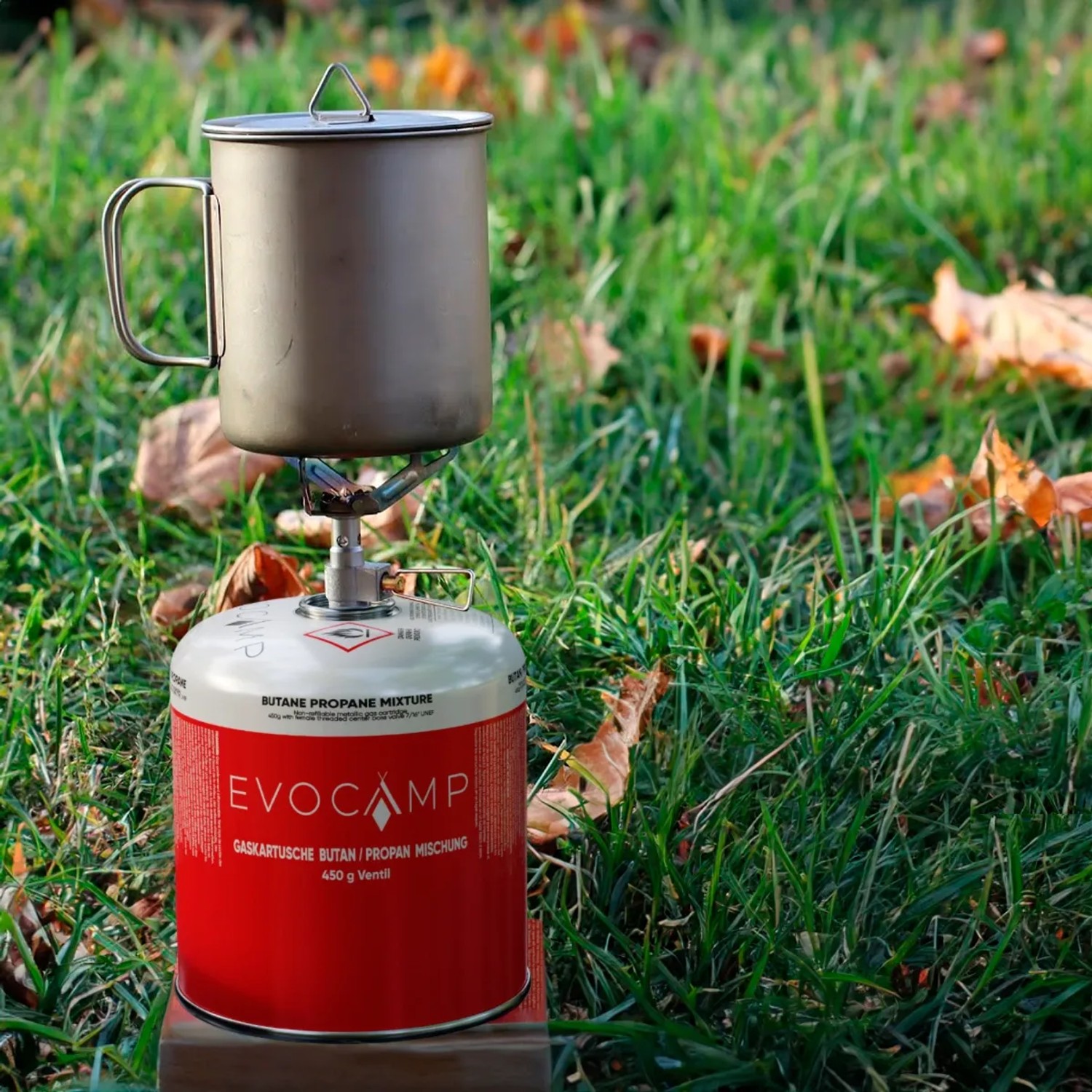 Evocamp Gaskartusche mit Campingkocher und Topf auf Rasen. Propan-Butan-Gemisch für Campingkocher.
