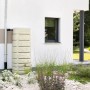 4rain Wandtank Slim Stone Decor 500 l, sandbeige, an Hauswand mit Regenrohr und Garten.