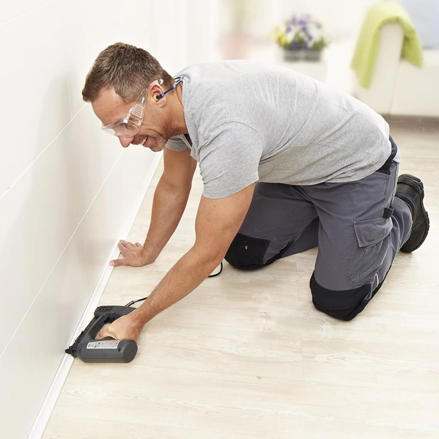 Mann befestigt Zierleiste mit Novus Elektrotacker J-165 Panel an Wand.