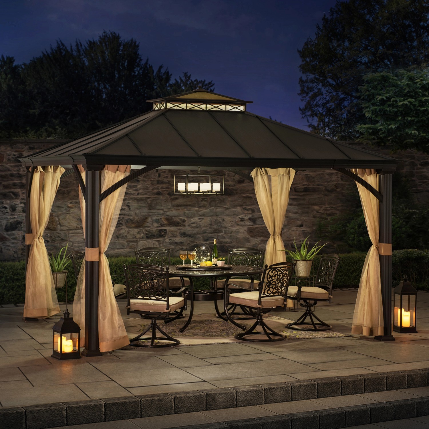 Schwarzer Sunjoy Gazebo Torre Zedernholz (385x324cm) mit Vorhängen und Gartenmöbeln bei Nacht.