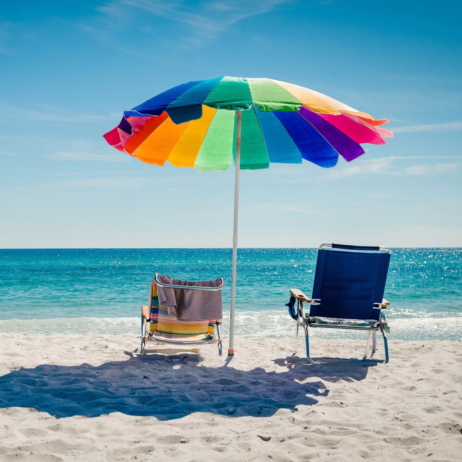 Strand-Szene mit buntem Sonnenschirm, zwei Liegestühlen und Meer.
