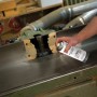 Hand sprüht Ballistol Holzgleitspray 400 ml auf Metalltisch einer Holzbearbeitungsmaschine in Werkstatt. Trockenschmierung.