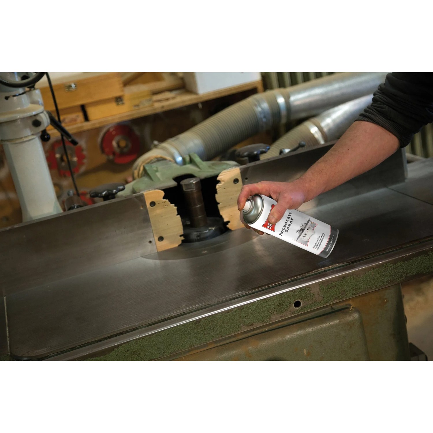 Hand sprüht Ballistol Holzgleitspray 400 ml auf Metalltisch einer Holzbearbeitungsmaschine in Werkstatt. Trockenschmierung.