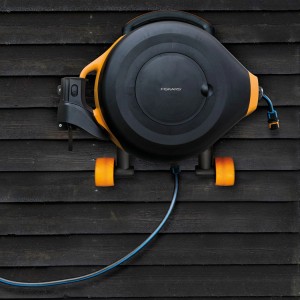 Fiskars Waterwheel XL Wandhalterung für Gartenschlauchwagen, schwenkbar und platzsparend an dunkler Holzwand.