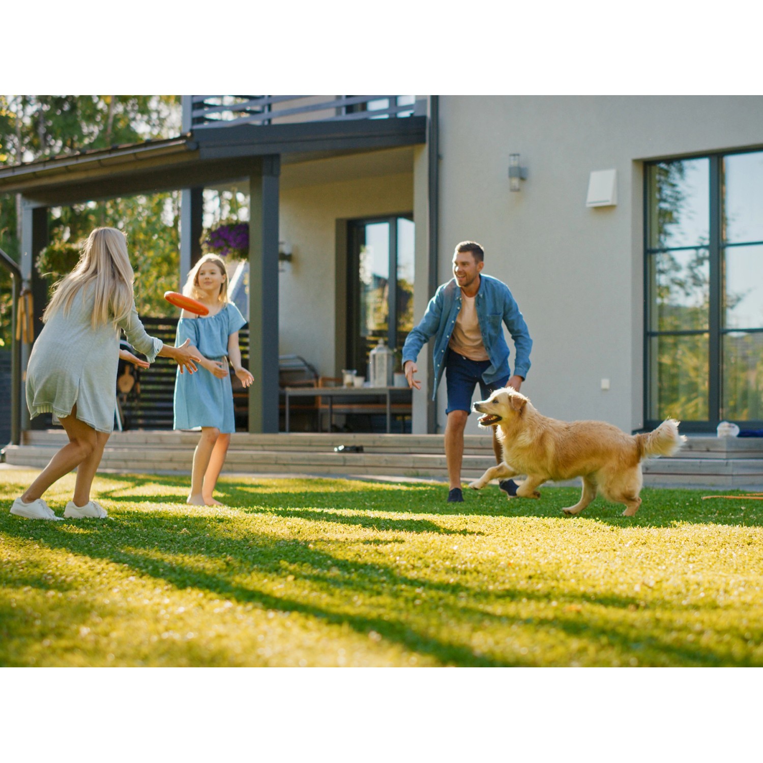 Familie spielt mit Hund auf Primaflor Kunstrasen Jazz Grün im Garten.