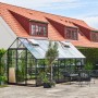 Schwarzes Halls Gewächshaus Qube+ 816 mit 13 m² im Garten, ausgestattet mit Sitzmöbeln.