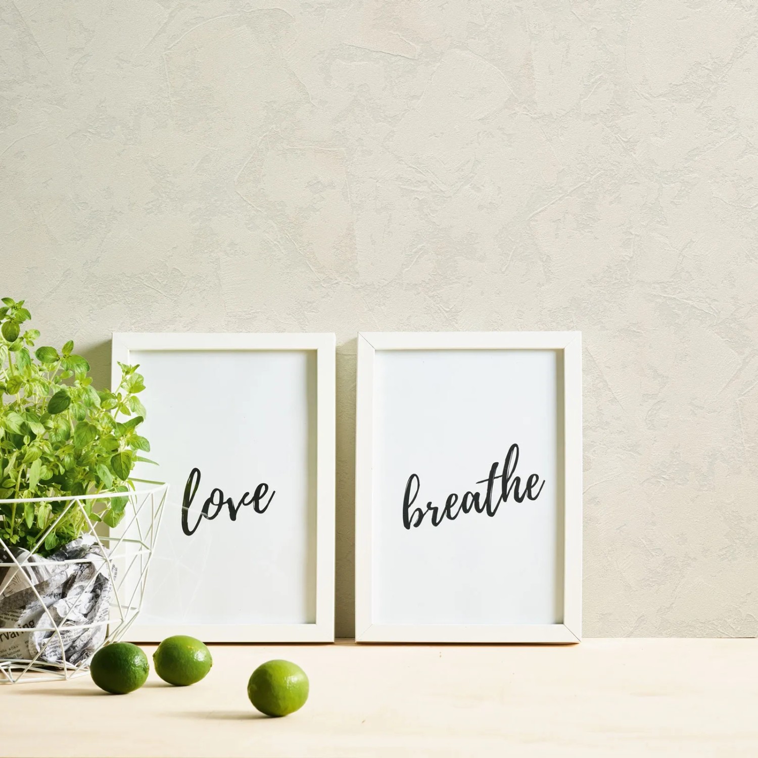 Helle Vliestapete in Putzoptik mit zwei weißen Bilderrahmen, einer mit "Love", einer mit "Breathe".