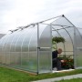 Silbernes Palram Canopia Bella Gewächshaus (4.8x2.4m) mit Stegplatten und geöffneter Tür.
