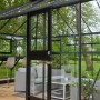 Juliana Gewächshaus Grand Oase 18 Anthrazit mit geöffneter Tür und Gartenmöbeln.