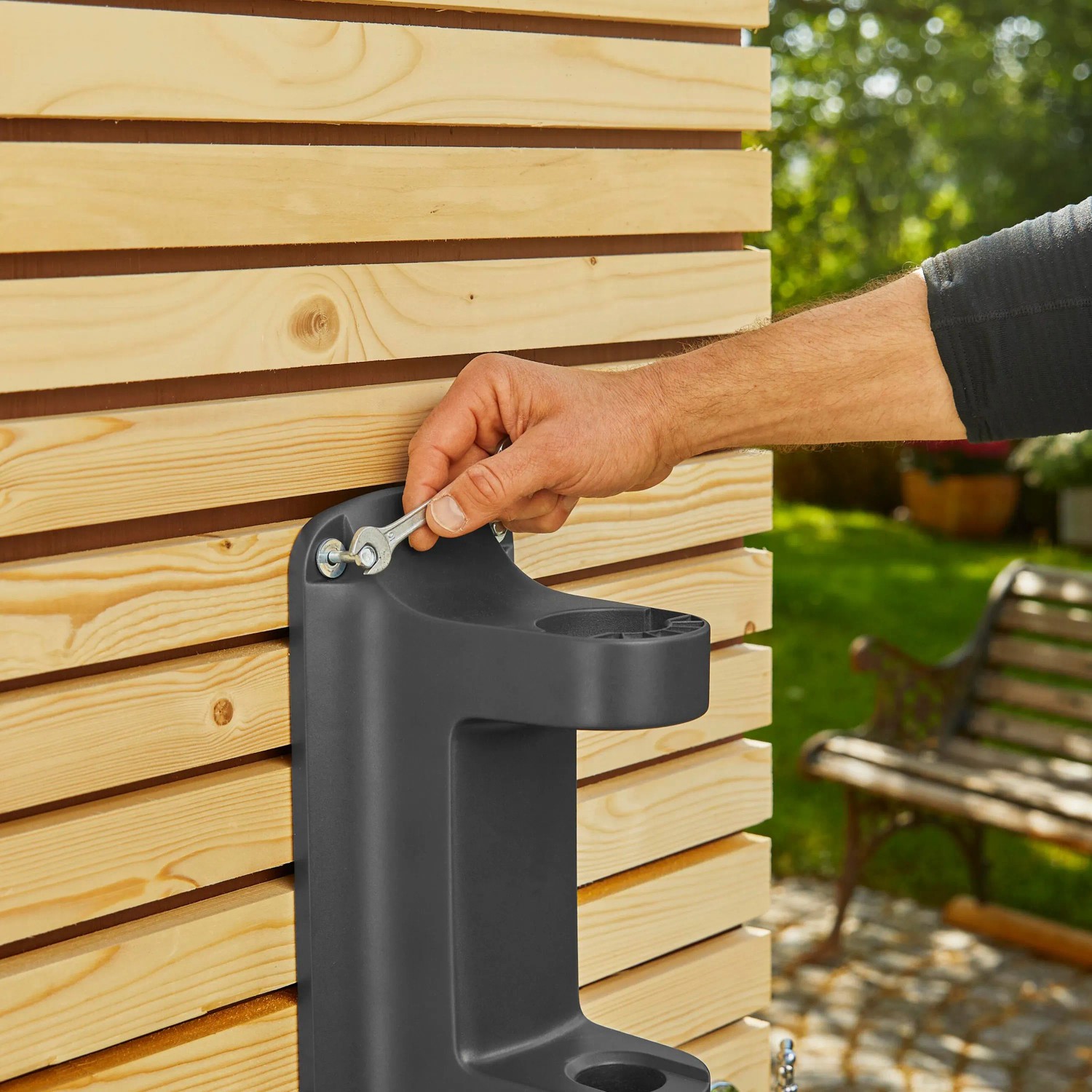 Montage der Gardena Wand-Schlauchbox XL an einer Holzwand mit Schraubenschlüssel.