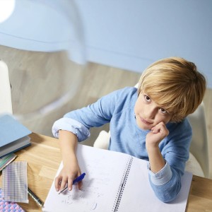 Blonder Junge am Schreibtisch mit Notizbuch, blickt nach oben. Perfekte Beleuchtung durch Philips Deckenleuchte.