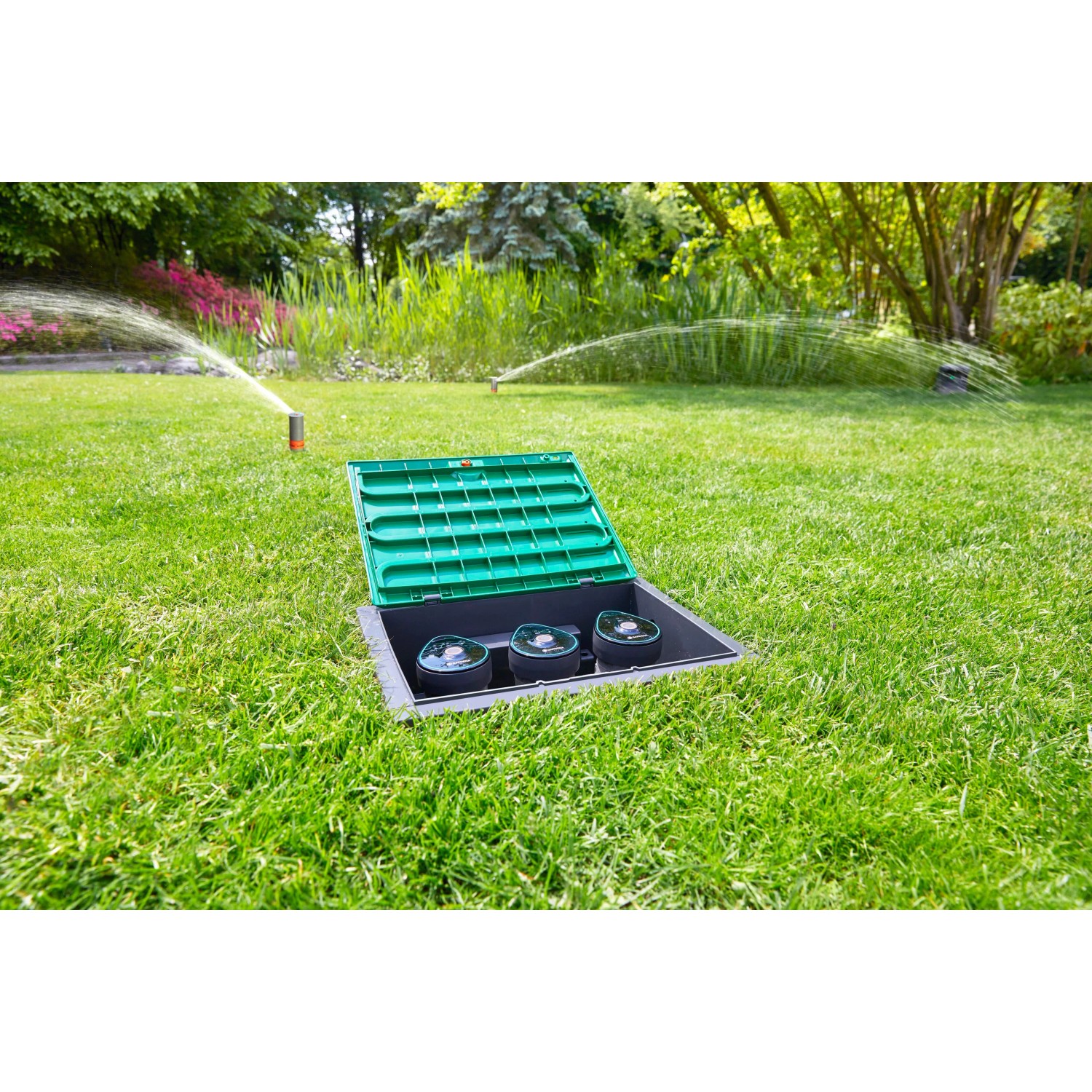 Gardena Bewässerungsventil 9 V Bluetooth im Garten mit geöffnetem Deckel und laufenden Sprengern.