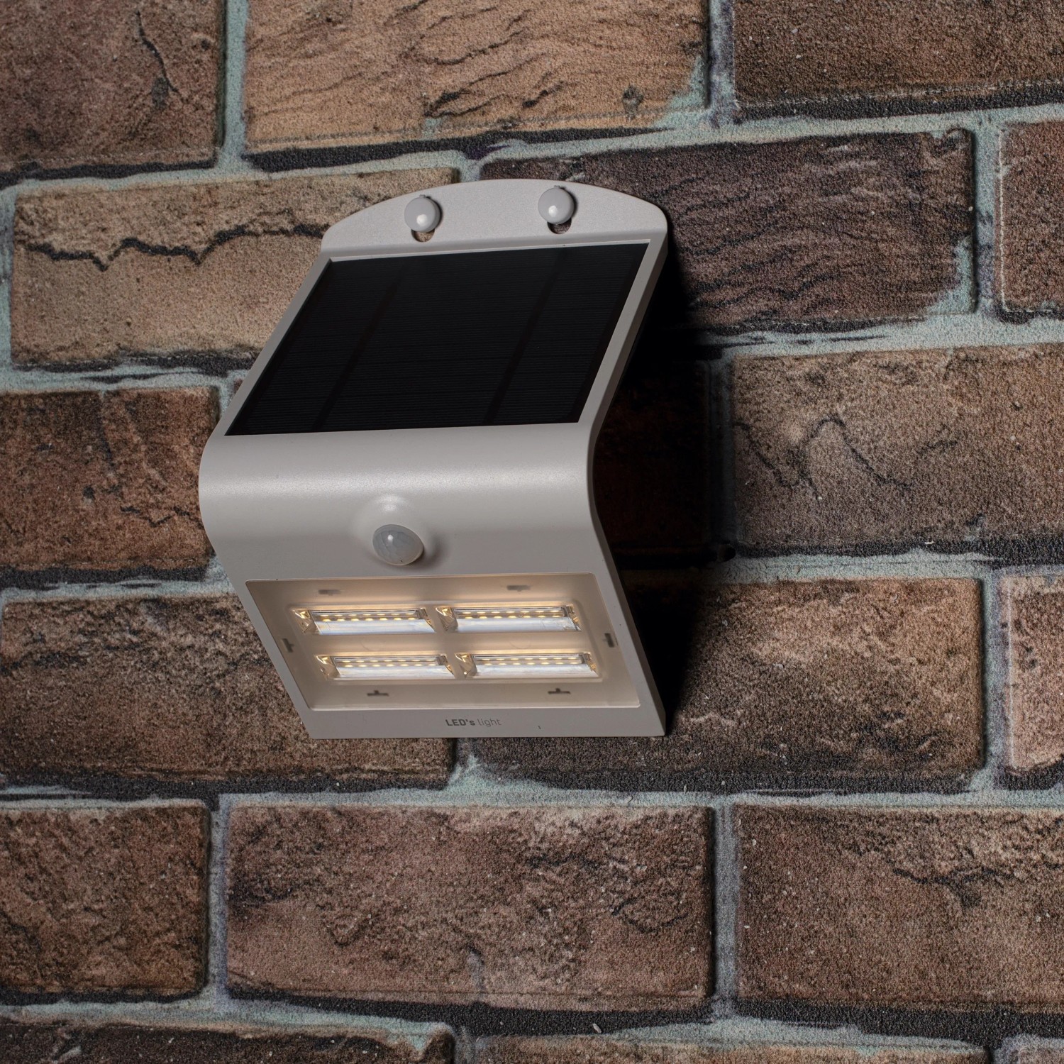 Weiße LED Solar-Außenleuchte mit Sensor an einer Backsteinwand. Flutlicht mit 400 Lumen.