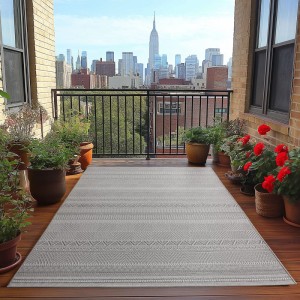 Grauer Ayyildiz Outdoor-Teppich Desert (120x170 cm) auf einem Balkon mit Stadtblick.