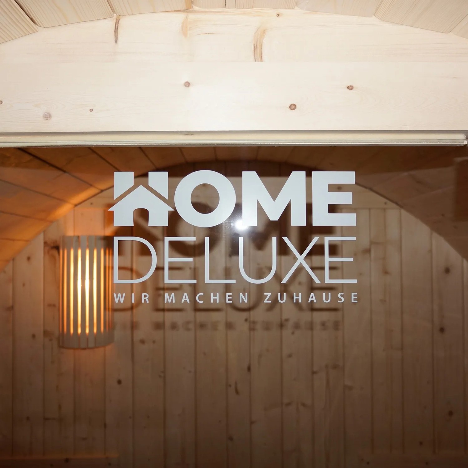 Detailaufnahme der Glastür der Home Deluxe Fasssauna Lahti Deluxe XL mit Logo und Innenansicht.