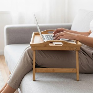 Person nutzt klappbares Bambus Betttablett natur mit Laptop auf Sofa. Ideal für Frühstück oder Homeoffice.