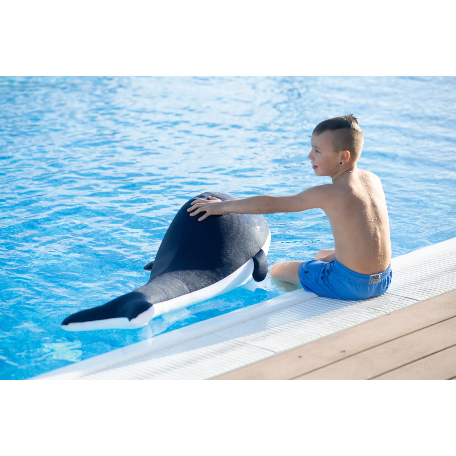 Junge streichelt blauen Westmann Pool Buddy Wal am Poolrand. Badespaß & Spielzeug.