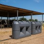 Zwei graue, marmorierte KMND 2000L Flach-Wassertanks mit Schlauchanschluss vor einem Kuhstall. Ideal für Trinkwasser & Garten.