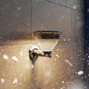 Schwarze Philips Solar-Außenwandleuchte Kyna (13,9x15,8x13,7 cm) an Hauswand im Schnee.