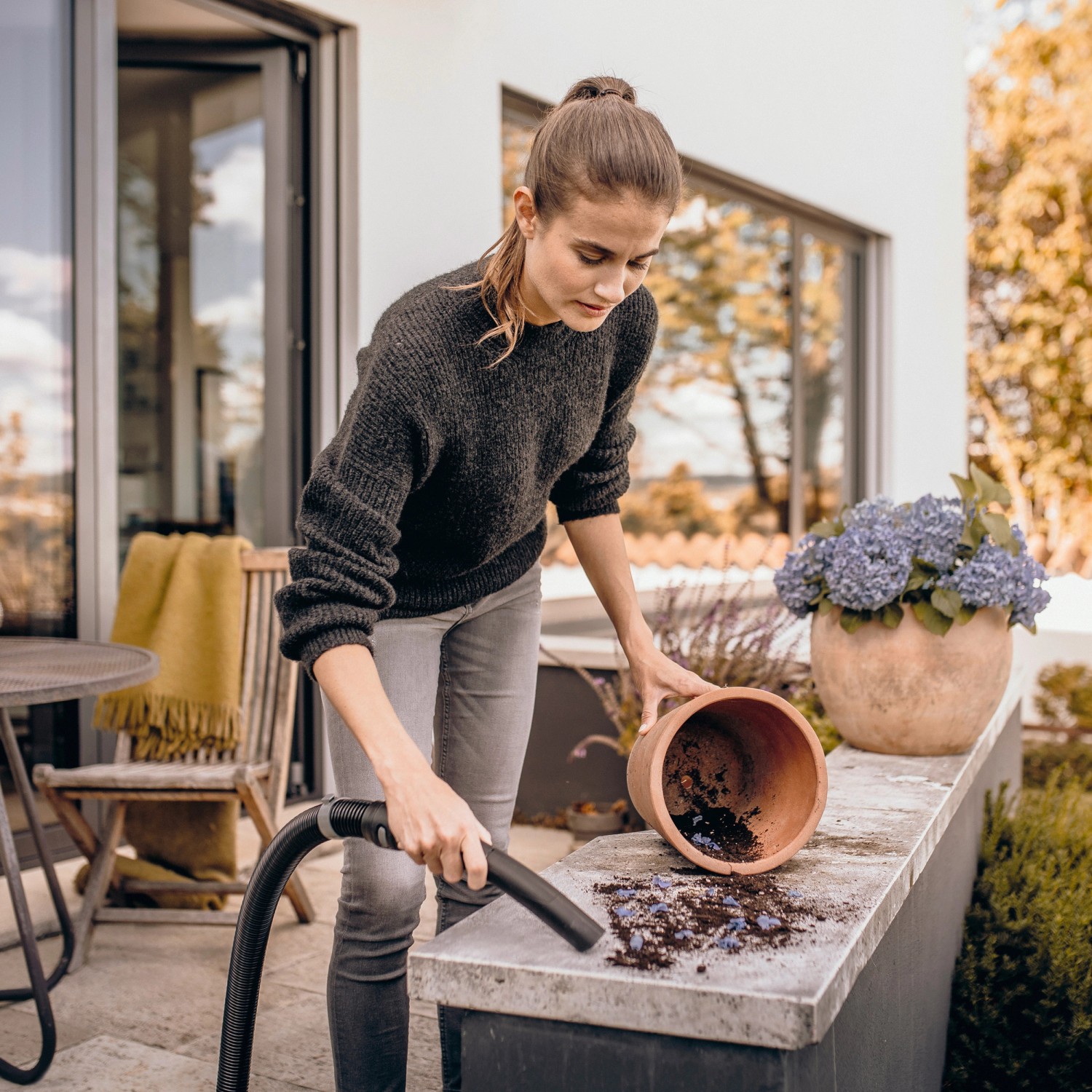 Frau saugt mit Kärcher WD 3 V-17/4/20 Nass-/Trockensauger Erde von einer Mauer.