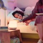 Weiße WiZ LED-Tischleuchte Hero neben Kind im Bett, gesteuert per App.