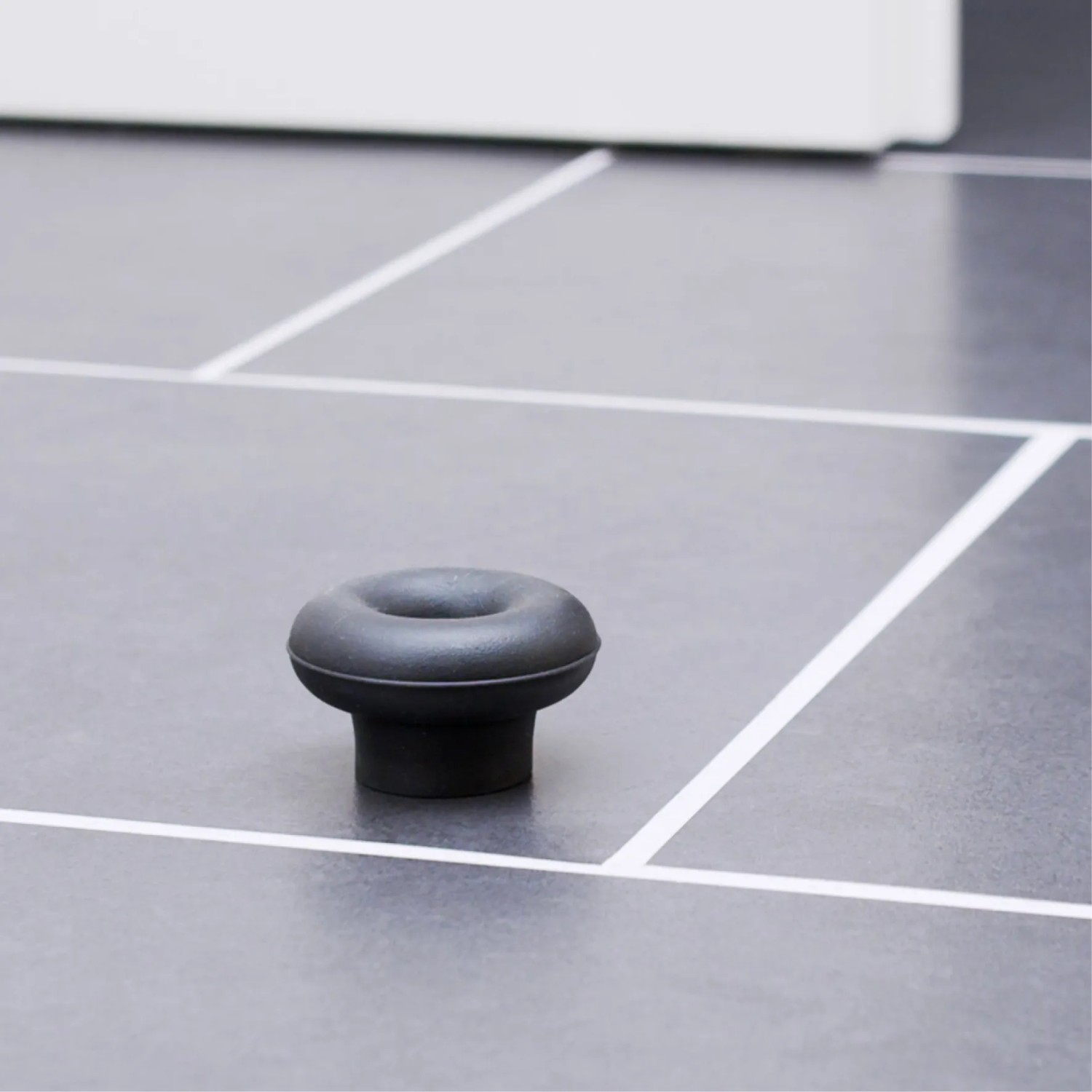 Schwarzer Wagner Bodentürstopper EH5201 aus Gummi auf grauem Fliesenboden.