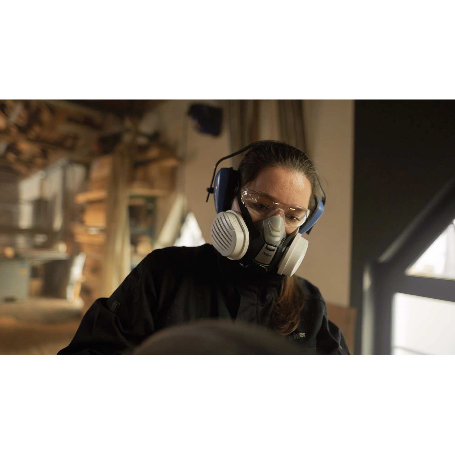 Frau mit Dräger Halbmaske X-plore 3300 Handwerkerset, P3-R-Filter, Schutzbrille und Kopfhörer beim Arbeiten.
