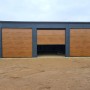 Liderstal Blechhalle Premium 12x8m mit drei Sektionaltoren in Goldene Eiche und graphitgrauen Wänden, ein Tor offen.