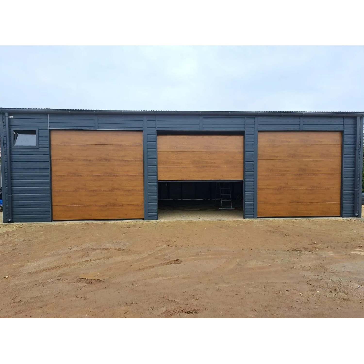 Liderstal Blechhalle Premium 12x8m mit drei Sektionaltoren in Goldene Eiche und graphitgrauen Wänden, ein Tor offen.