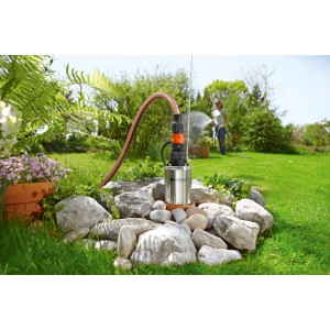 Gardena Premium Tiefbrunnenpumpe 6000/5 inox im Garten mit Schlauch und Bewässerung im Hintergrund.