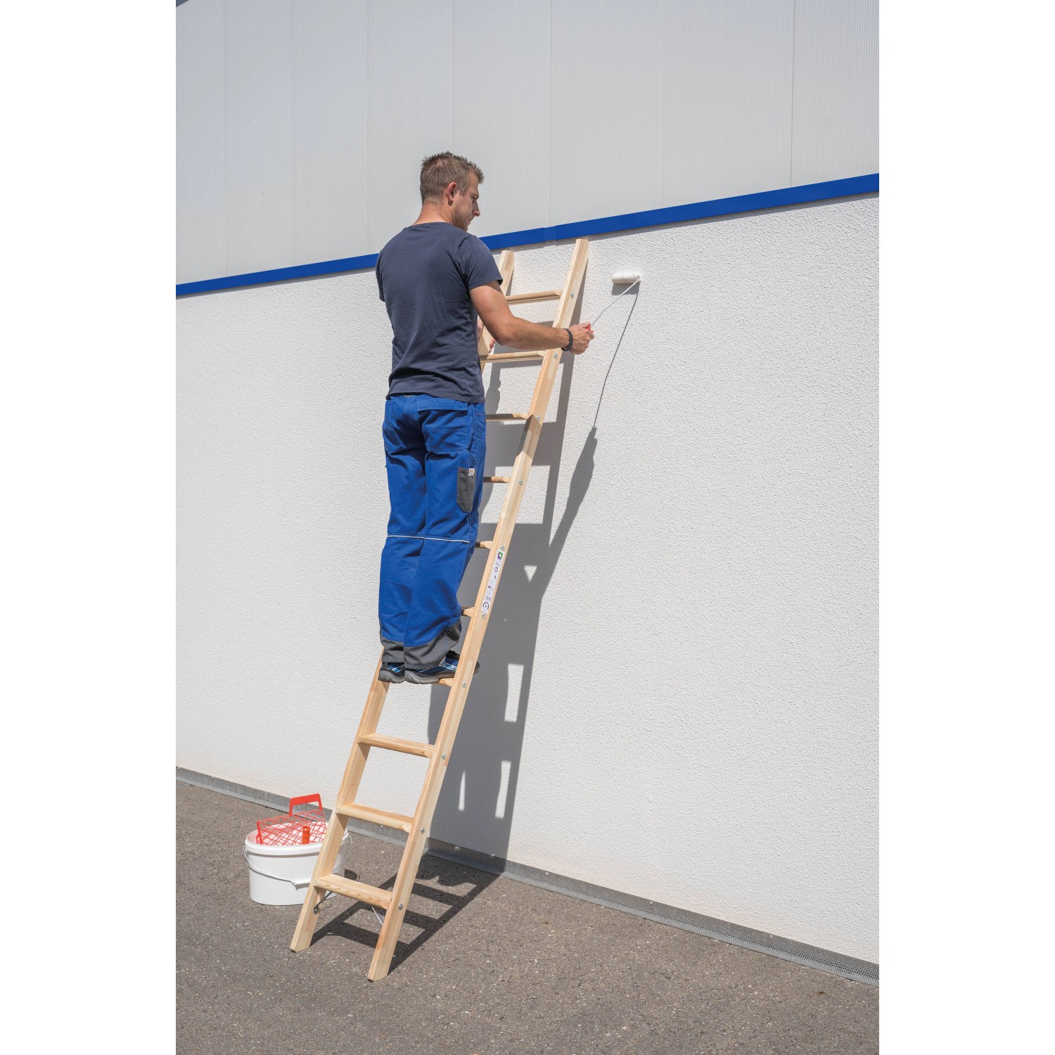 Mann streicht Wand mit PROREGAL Holz-Anlegeleiter (8 Stufen) und Farbrolle.