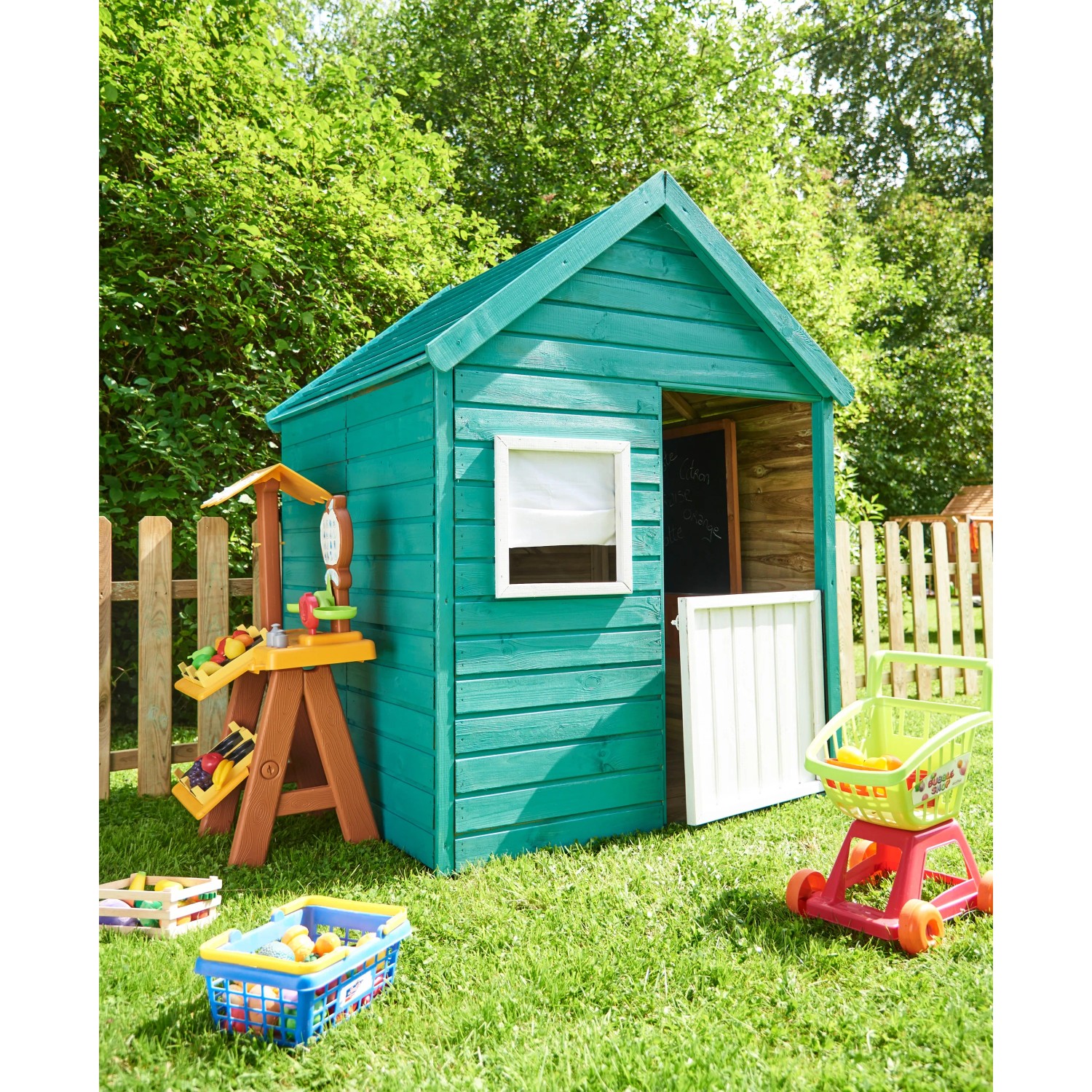 Grünes Soulet Kinderspielhaus Marina mit Fenster, halber Tür und Spielzeug auf einer grünen Wiese.