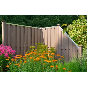 Brauner WPC-Sichtschutzzaun Shanghai (180x180 cm) im Garten mit Blumen.