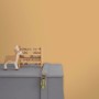 Wand in Ockergelb (Faded Ochre) von Little Dutch mit Spielzeug auf einer grauen Truhe.