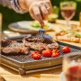 Ooni Grillpfanne Dual-Sided Grizzler mit Steak und Tomaten auf einem Gartentisch.