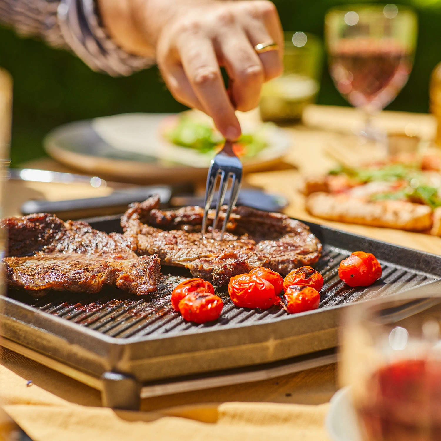 Ooni Grillpfanne Dual-Sided Grizzler mit Steak und Tomaten auf einem Gartentisch.