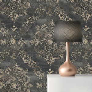 Graue Vliestapete mit barockem Ornamentmuster in Beige/Gold, leicht strukturiert. Eine Lampe steht davor.