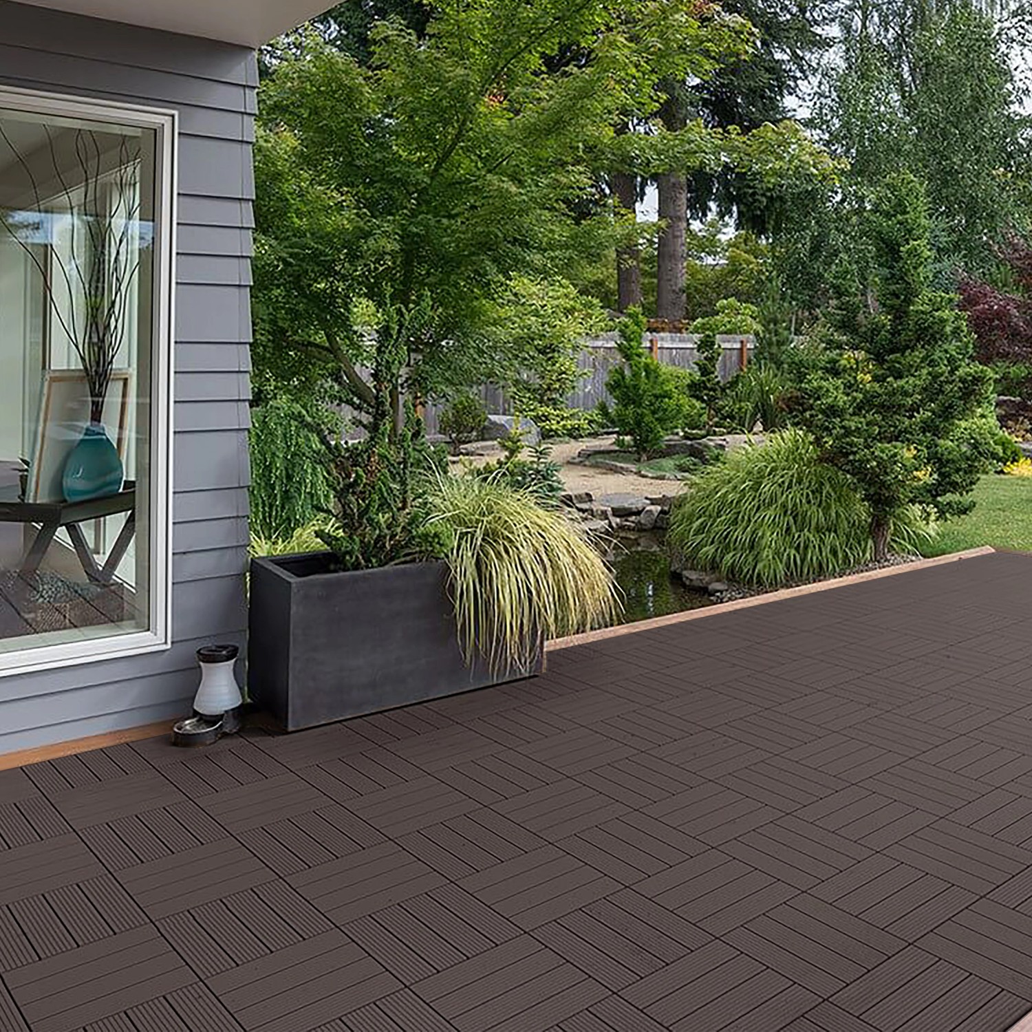 Verlegte Home Deluxe WPC Klickfliesen Bavaro, dunkelbraun, auf Terrasse mit Garten im Hintergrund.