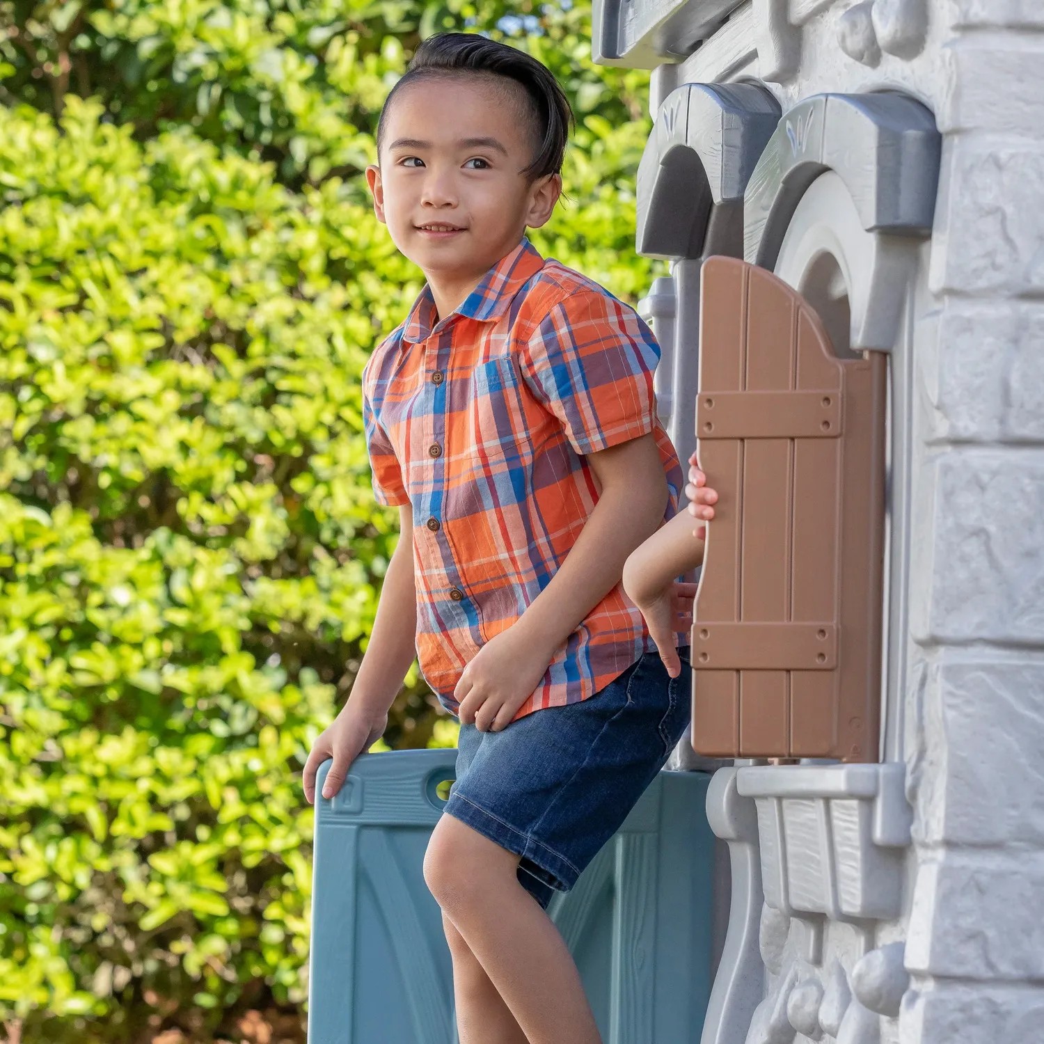 Kind im Step2 Adventures Spielhaus mit Rutsche, 2-stöckig, mit Bauernhoftüren und Fensterläden.