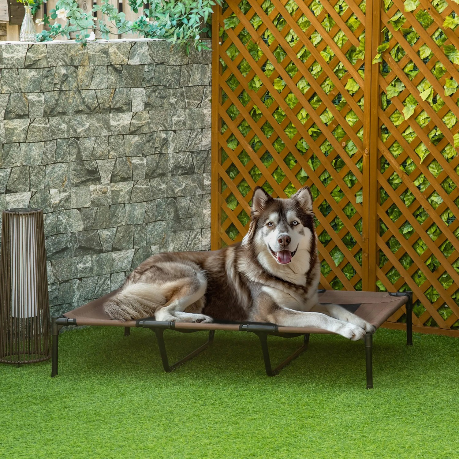 Hund liegt entspannt auf erhöhtem PawHut Hundebett/Hundesofa im Garten.