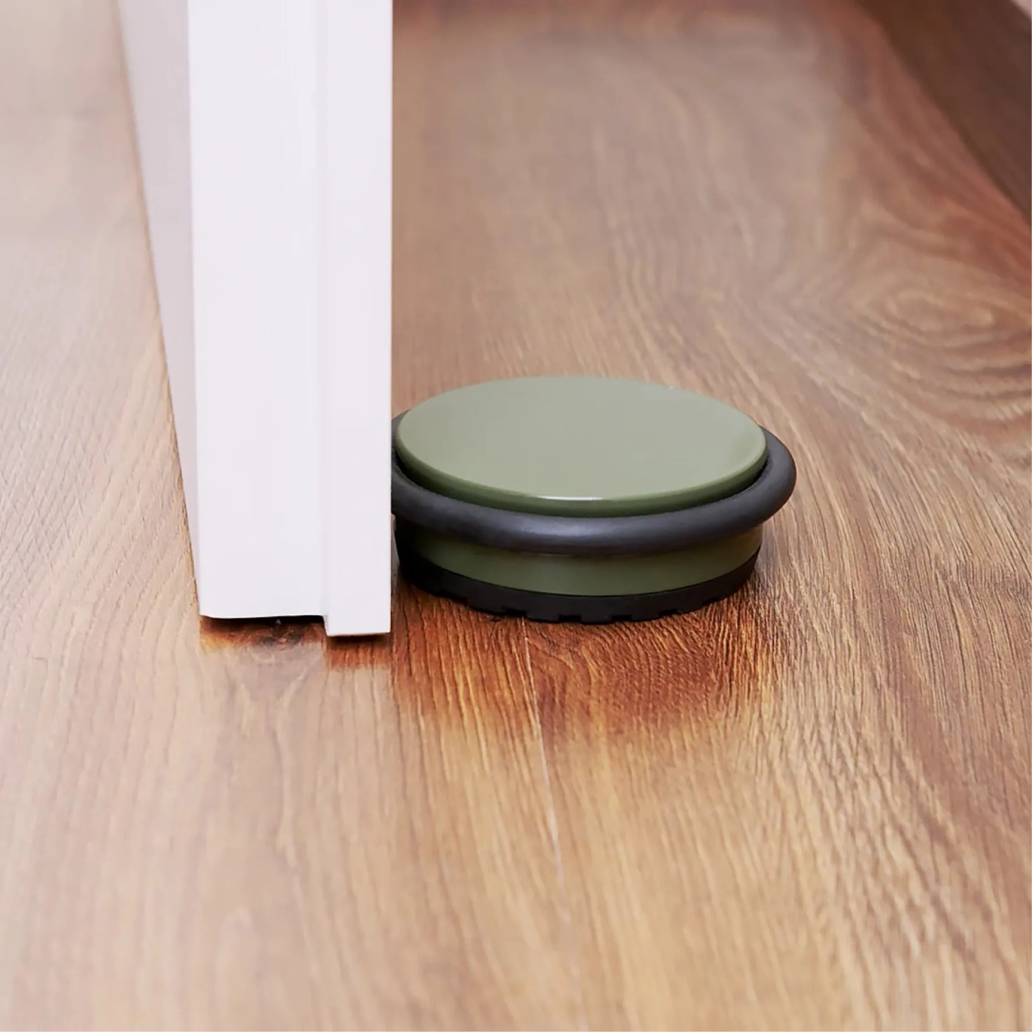 Olivgrüner Wagner Bodentürstopper Big Disk Color aus Stahl neben einer Tür auf Holzboden.