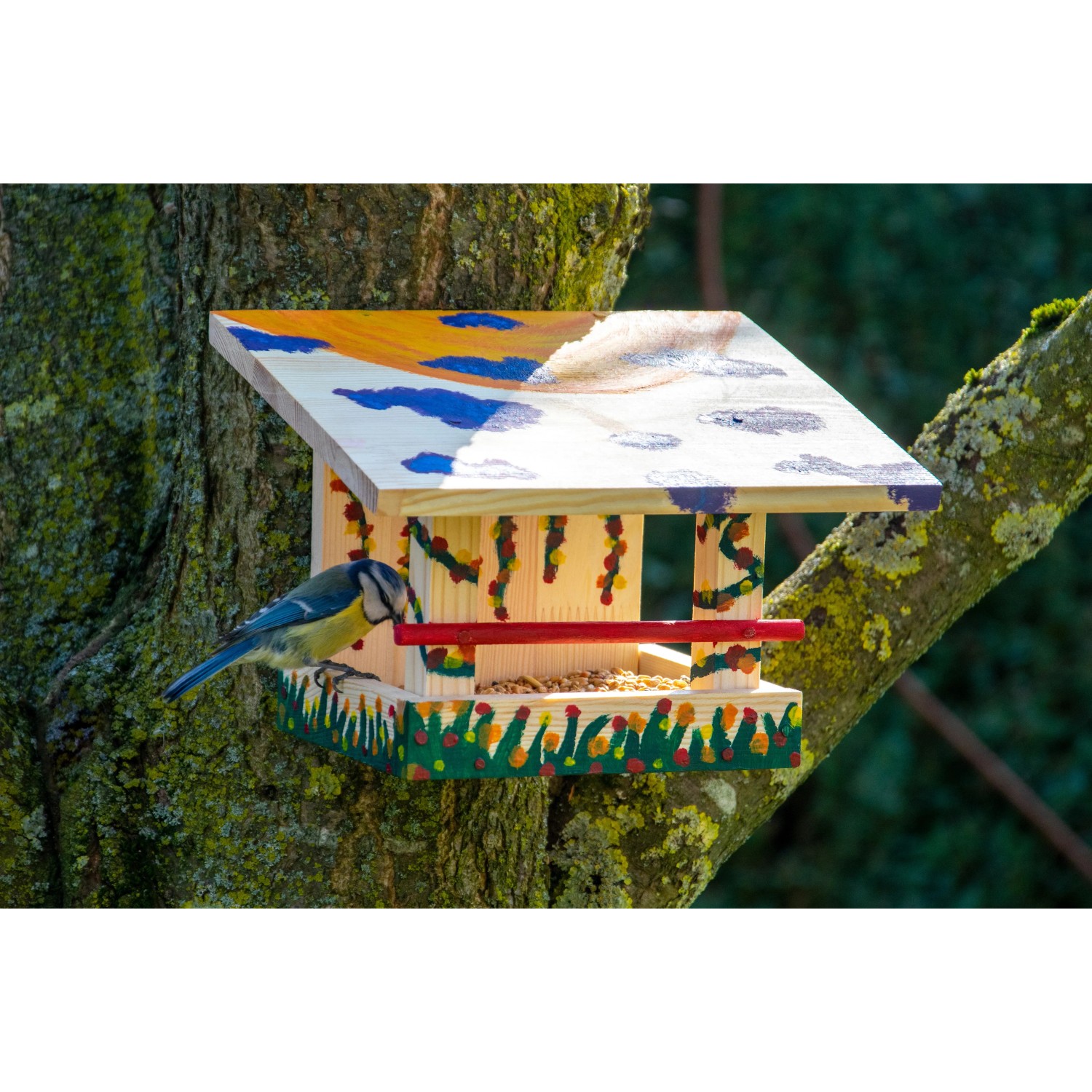 Bemaltes Dobar Vogelfutterhaus aus Kiefernholz mit Blaumeise am Baum.